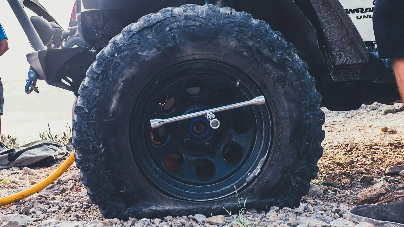 A wheel and a wheel brace on rough ground beside a vehicle.